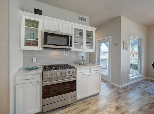 kitchen featuring a textured ceiling, light wood-type flooring, appliances with stainless steel finishes, decorative backsplash, and white cabinets