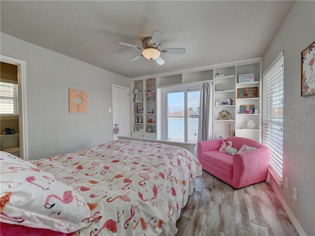 bedroom featuring a textured ceiling, light hardwood / wood-style flooring, ceiling fan, and a water view