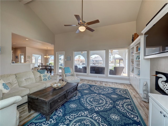 living room featuring a tile fireplace, ceiling fan with notable chandelier, high vaulted ceiling, and light hardwood / wood-style floors