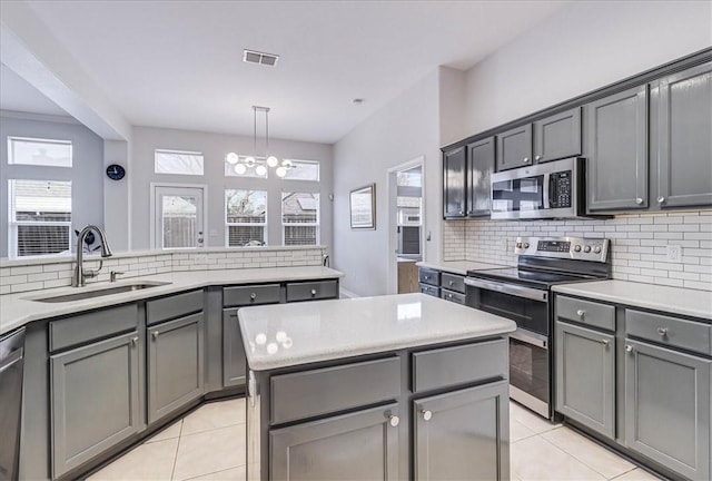 kitchen featuring a center island, stainless steel appliances, light countertops, gray cabinetry, and a sink