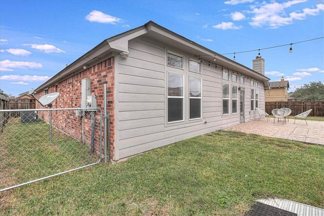 view of side of property featuring brick siding, a chimney, a lawn, a patio area, and a fenced backyard