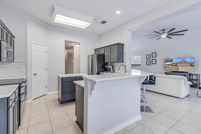 kitchen featuring light countertops, visible vents, gray cabinetry, appliances with stainless steel finishes, and a kitchen breakfast bar