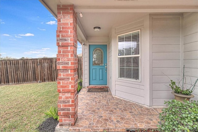 property entrance with a yard, fence, and brick siding