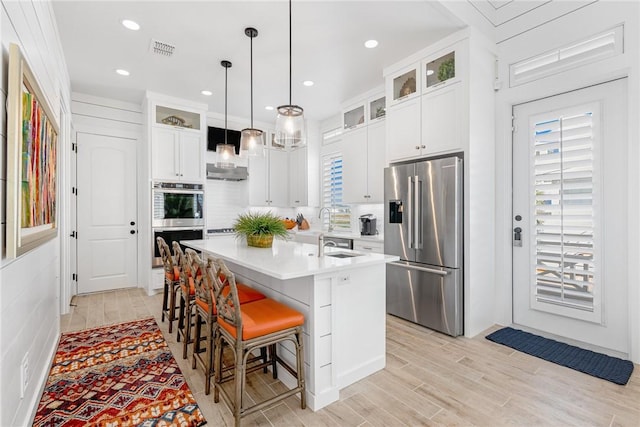 kitchen featuring a breakfast bar, a center island with sink, white cabinets, light hardwood / wood-style floors, and stainless steel appliances