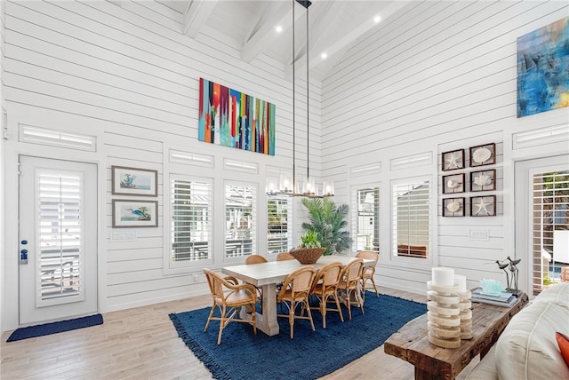 dining room with beamed ceiling, wooden walls, high vaulted ceiling, and light hardwood / wood-style flooring