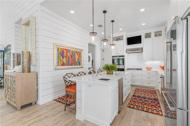 kitchen with stacked washer / dryer, sink, white cabinetry, and a kitchen island with sink