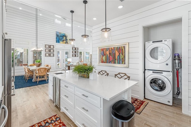 kitchen featuring stainless steel refrigerator, white cabinetry, pendant lighting, stacked washer / drying machine, and a kitchen island