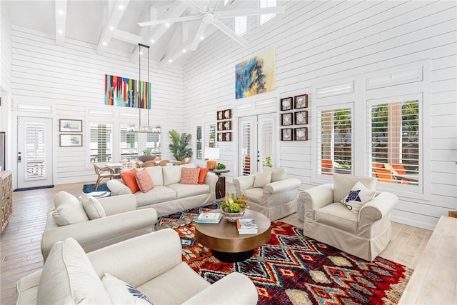 living room with light wood-type flooring, ceiling fan with notable chandelier, beam ceiling, high vaulted ceiling, and wood walls