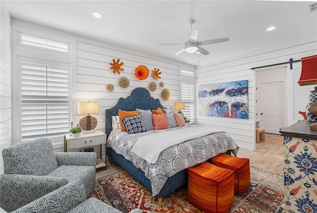 bedroom featuring light wood-type flooring, a barn door, ceiling fan, and wooden walls