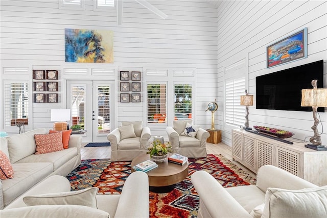 living room featuring a high ceiling, hardwood / wood-style flooring, french doors, and wood walls