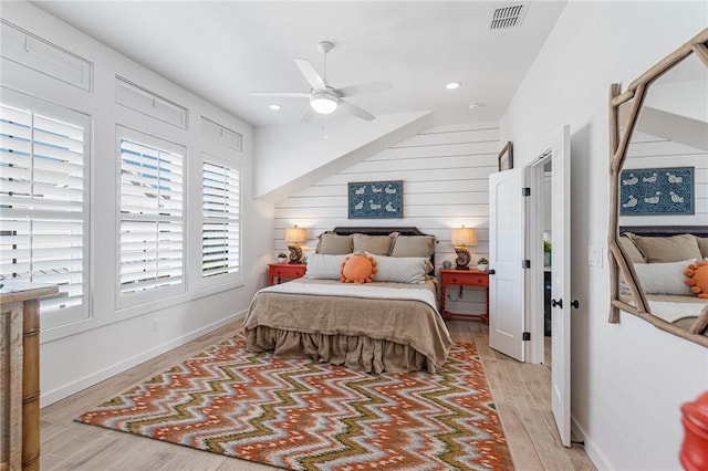 bedroom featuring ceiling fan, wood walls, light wood-type flooring, and multiple windows