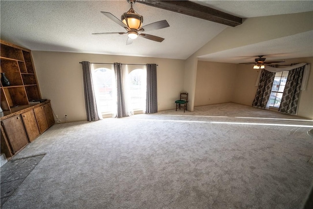 unfurnished living room featuring a wealth of natural light, ceiling fan, lofted ceiling with beams, and a textured ceiling