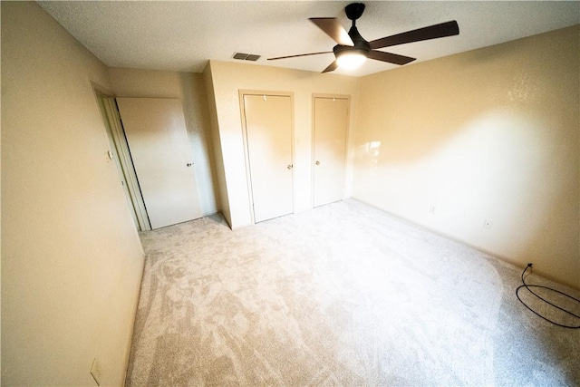 unfurnished bedroom with light colored carpet, ceiling fan, and multiple closets