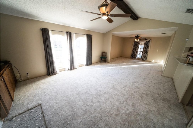 unfurnished living room with ceiling fan, lofted ceiling with beams, a textured ceiling, and a wealth of natural light