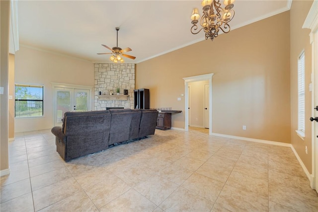 living room featuring light tile patterned floors, crown molding, a stone fireplace, baseboards, and ceiling fan with notable chandelier