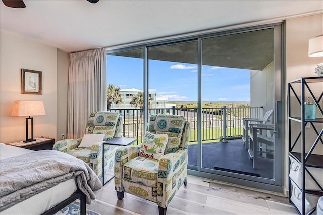 bedroom featuring light hardwood / wood-style floors, access to exterior, a wall of windows, and multiple windows