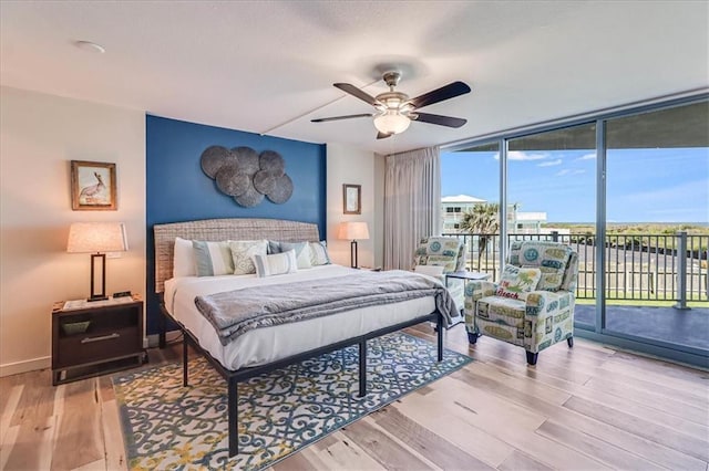 bedroom with access to exterior, ceiling fan, a wall of windows, and light wood-type flooring