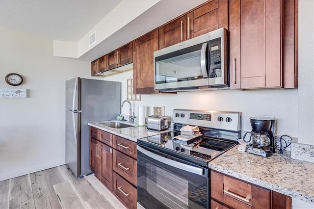 kitchen with light stone countertops, stainless steel appliances, light hardwood / wood-style flooring, and sink