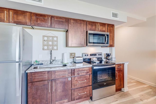 kitchen with light stone counters, light wood-type flooring, sink, and appliances with stainless steel finishes