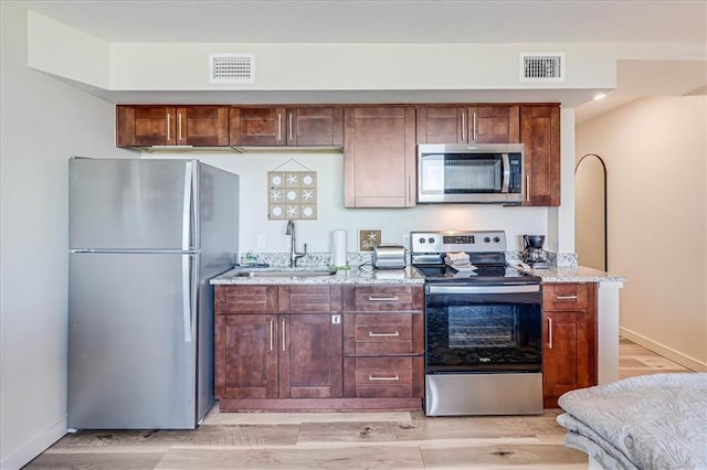 kitchen with light wood-type flooring, stainless steel appliances, light stone counters, and sink