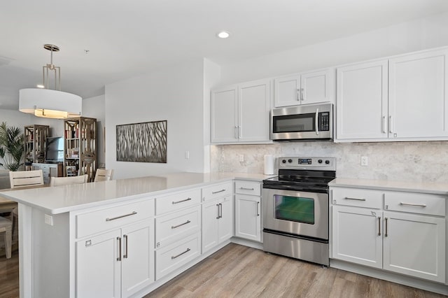 kitchen featuring kitchen peninsula, appliances with stainless steel finishes, decorative light fixtures, and light hardwood / wood-style flooring