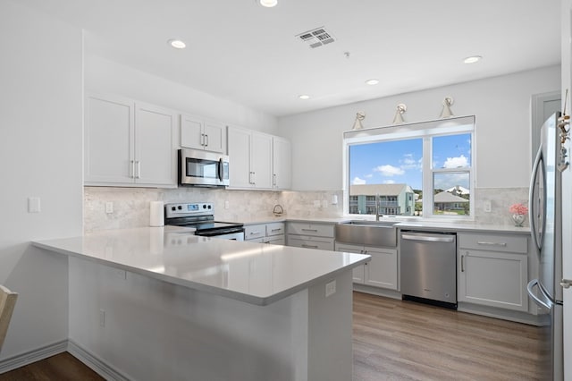 kitchen featuring kitchen peninsula, light wood-type flooring, stainless steel appliances, and white cabinetry