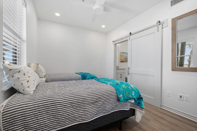 bedroom featuring a barn door, ceiling fan, and hardwood / wood-style floors