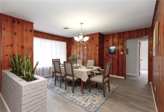 dining room featuring wood walls, light wood-type flooring, and a notable chandelier