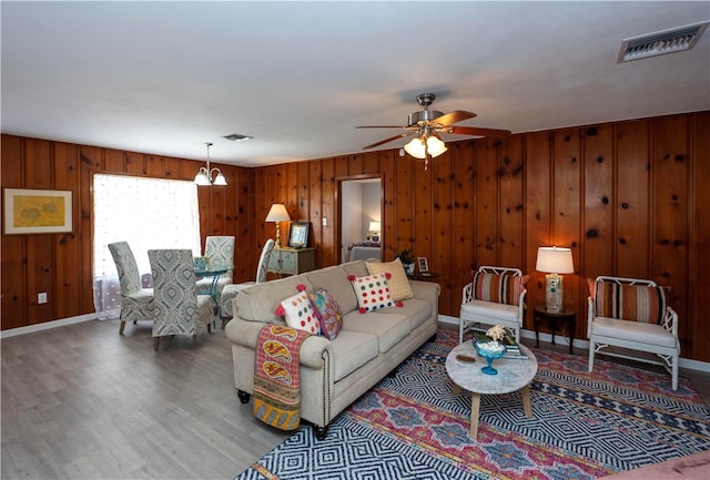 living room featuring wooden walls, hardwood / wood-style floors, and ceiling fan with notable chandelier