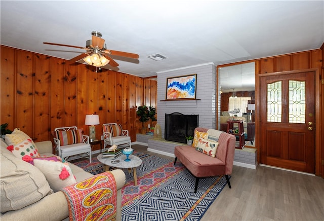 living room with a fireplace, ceiling fan, wood walls, and light wood-type flooring