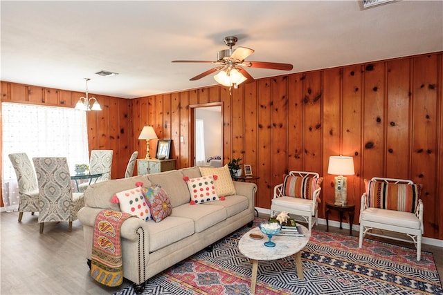 living room with wooden walls, wood-type flooring, and ceiling fan with notable chandelier