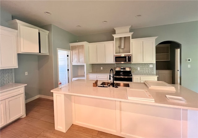 kitchen featuring a kitchen island with sink, white cabinetry, stainless steel appliances, tasteful backsplash, and light hardwood / wood-style floors