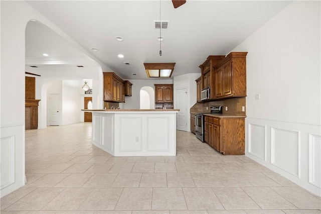 kitchen featuring arched walkways, a decorative wall, stainless steel appliances, visible vents, and tasteful backsplash