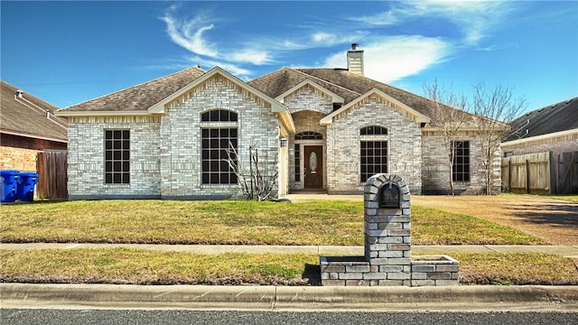 french country style house with a front yard, brick siding, fence, and roof with shingles