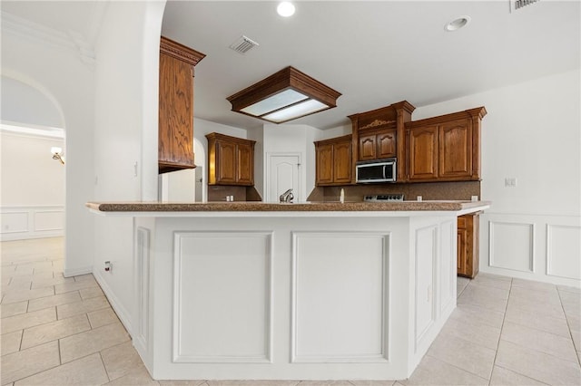 kitchen with visible vents, stainless steel microwave, a decorative wall, and light tile patterned flooring