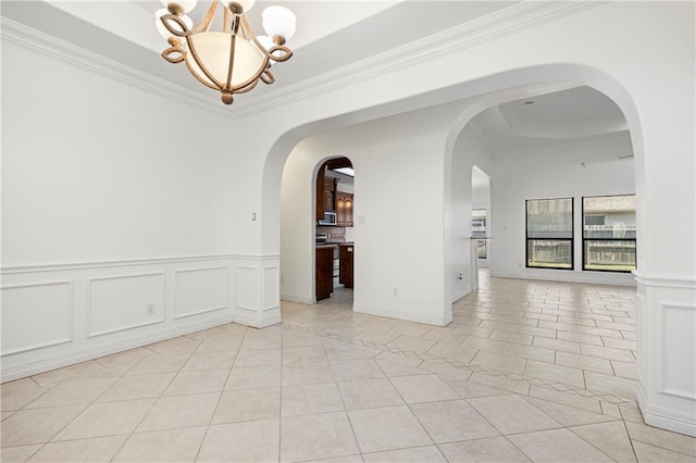 empty room featuring arched walkways, crown molding, a notable chandelier, a decorative wall, and light tile patterned flooring