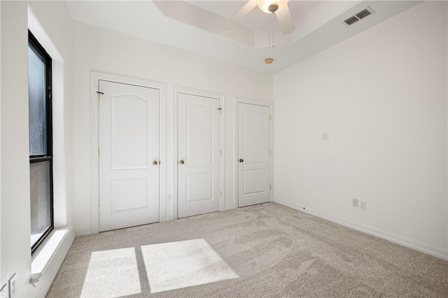 unfurnished bedroom featuring baseboards, a raised ceiling, visible vents, and light colored carpet