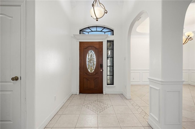 entrance foyer featuring arched walkways, wainscoting, a decorative wall, and light tile patterned floors