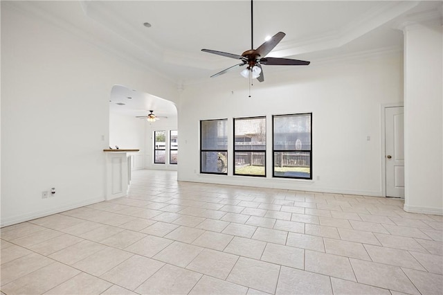 unfurnished living room with light tile patterned floors, arched walkways, a raised ceiling, and ornamental molding