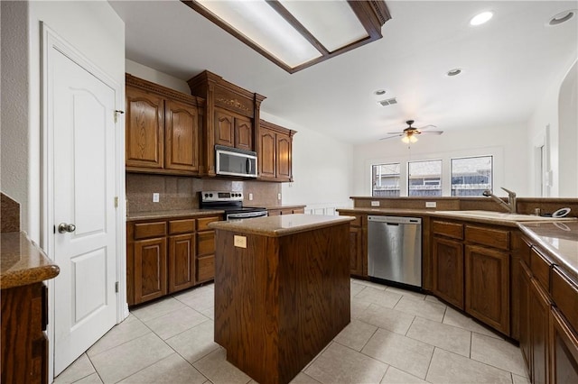 kitchen featuring appliances with stainless steel finishes, light tile patterned flooring, a sink, ceiling fan, and a kitchen island