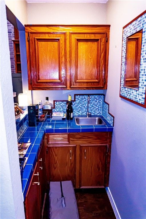 kitchen featuring a sink, backsplash, baseboards, brown cabinetry, and dark wood-style flooring