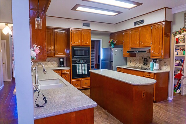 kitchen featuring visible vents, a sink, under cabinet range hood, black appliances, and dark wood-style flooring