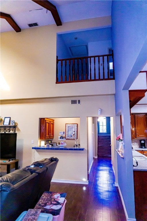 living area featuring visible vents, baseboards, a towering ceiling, and dark wood-style flooring