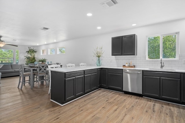 kitchen with sink, kitchen peninsula, backsplash, stainless steel dishwasher, and light hardwood / wood-style flooring