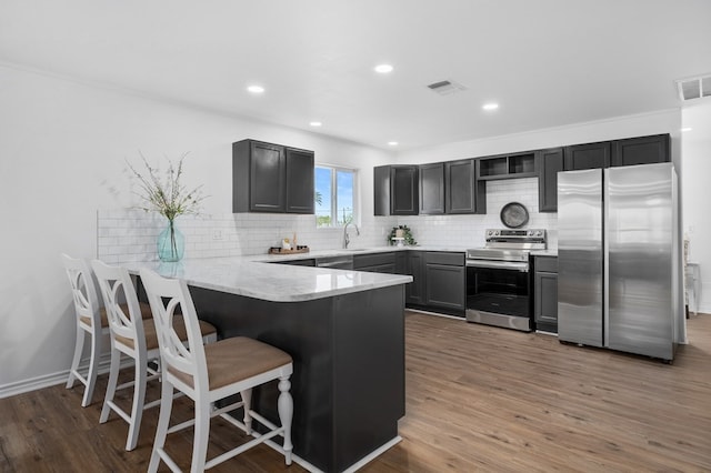 kitchen with kitchen peninsula, appliances with stainless steel finishes, dark wood-type flooring, and backsplash