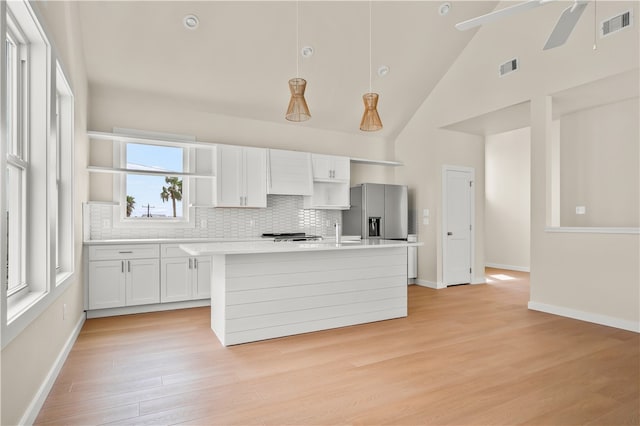 kitchen with stainless steel refrigerator with ice dispenser, hanging light fixtures, a kitchen island with sink, high vaulted ceiling, and white cabinetry