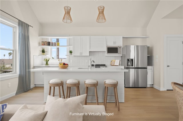 kitchen with pendant lighting, stainless steel appliances, white cabinets, and vaulted ceiling