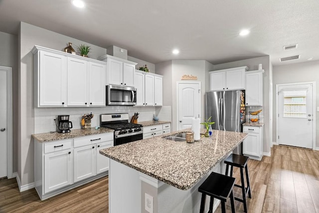 7753 Lariat Toss Dr, Corpus Christi, TX 78414 - kitchen with appliances with stainless steel finishes, wood finished floors, a kitchen island with sink, white cabinets, and recessed lighting