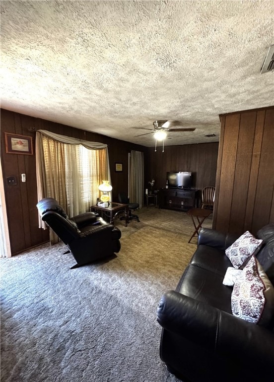 living room with wood walls, carpet, ceiling fan, and a textured ceiling