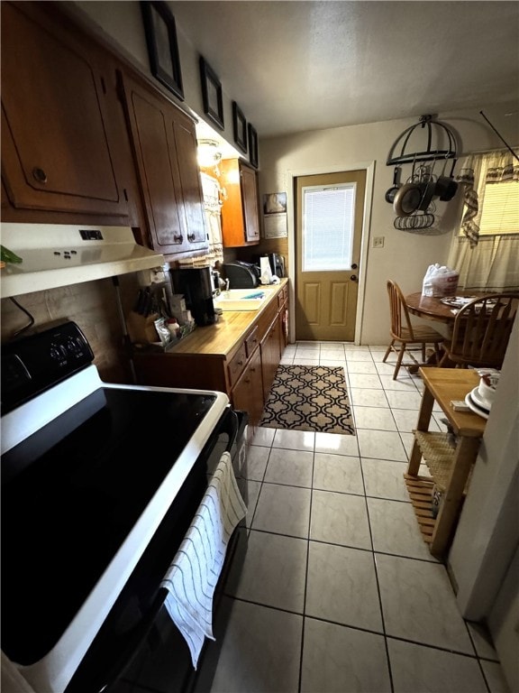 kitchen featuring electric stove, butcher block countertops, range hood, a sink, and light tile patterned flooring